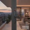 Cuerpo exterior oscuro de un panel biométrico instalado en el marco metálico delgado de una puerta corrediza de cristal con vista panorámica a la ciudad al atardecer.